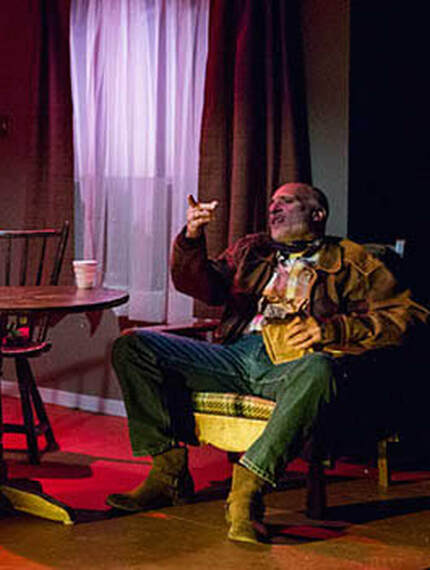 A man sits in an armchair smoking a cigar in Fool for Love.